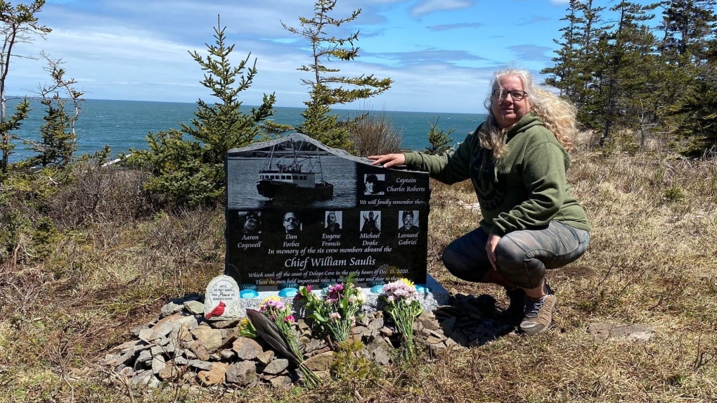 Lori Phillips crouches alongside a monument on Tuesday, May 10, 2022 in Delap's Cove, N.S. remembering her son Aaron Phillips and other members of the crew of the Chief William Saulis. (THE CANADIAN PRESS/Lori Phillips)