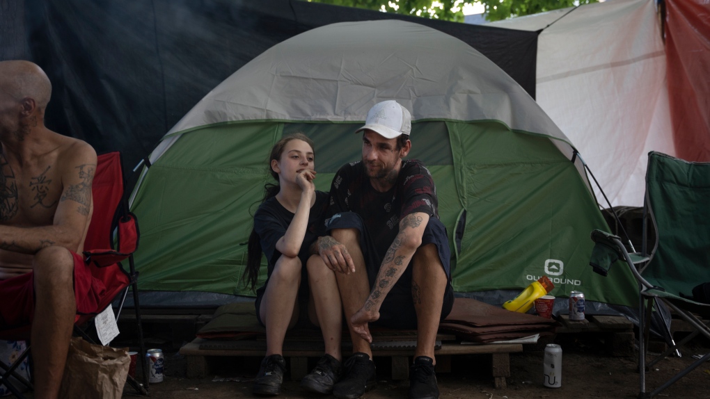 Emily, left, who wished not to give her last name, and her partner share a moment while sitting with others in their community living unhoused at Meagher Park in Halifax on Thursday, August 4, 2022. THE CANADIAN PRESS/Darren Calabrese