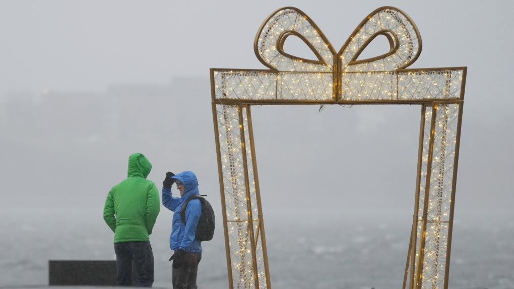 Pedestrians try to shield themselves from heavy wind and rain on the waterfront in Halifax on Friday, December 23, 2022. (THE CANADIAN PRESS/Darren Calabrese)